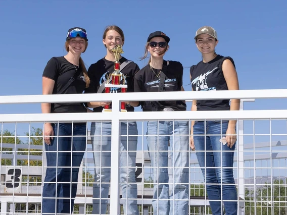 Four students stand smiling with one holding a trophy