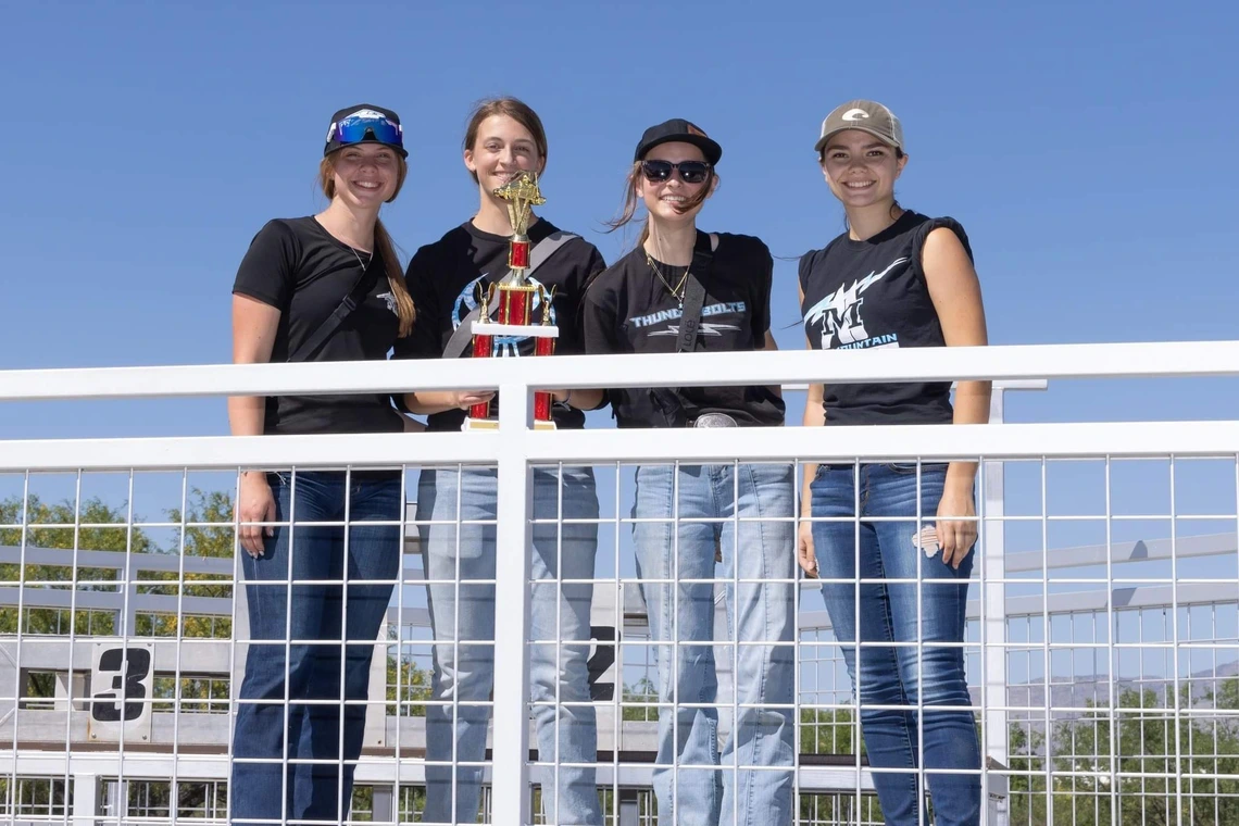 Four students stand smiling with one holding a trophy
