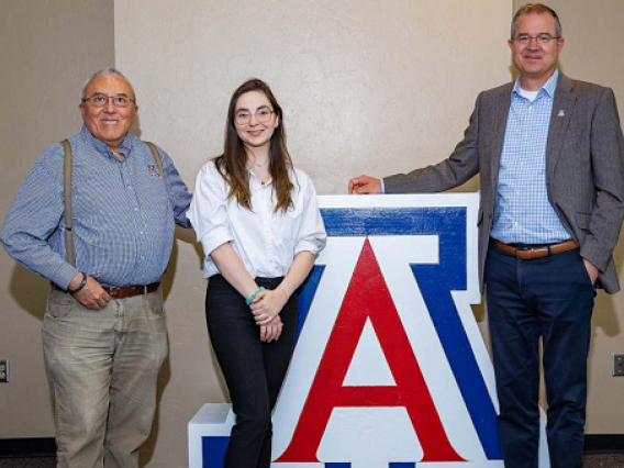 three people standing next to UA block A logo