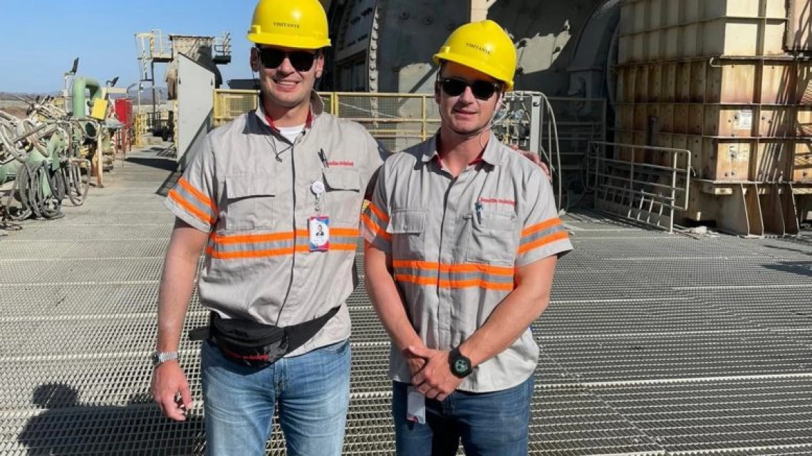 Adam and Jack Lundin are wearing hard hats and posing at a mining site