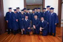A group of people wearing blue graduation caps and gowns smiles for a photo.