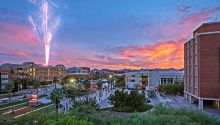 a photo of the busy University of Arizona mall at sunset, with a firework going off in the background on the left side.